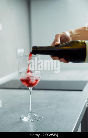 Die Hand einer Frau gießt zu Hause Rotwein in Gläser mit Eis Stockfoto