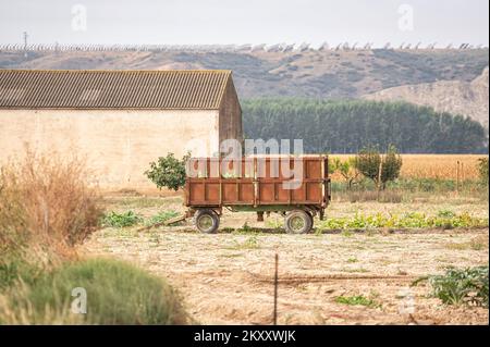 Ländliches Bild eines landwirtschaftlichen Zugmaschinenanhängers, der auf einem Feld in der Nähe eines Schuppens geparkt ist Stockfoto