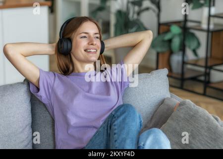 Zu Hause entspannen, positiv denken. Porträt einer glücklichen jungen Kaukasierin mit Kopfhörern, die ihre Lieblingsmusik hört Stockfoto