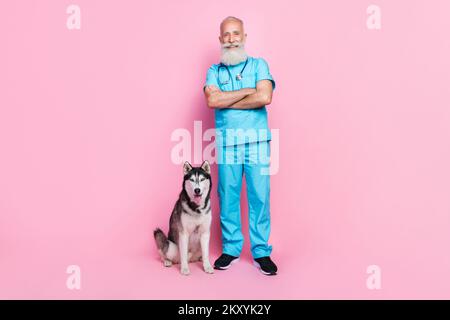 Großes Foto eines positiv zufriedenen älteren Mannes trägt blaue Uniform Hand gekreuzte Husky Haustier sitzt isoliert auf pinkfarbenem Hintergrund Stockfoto