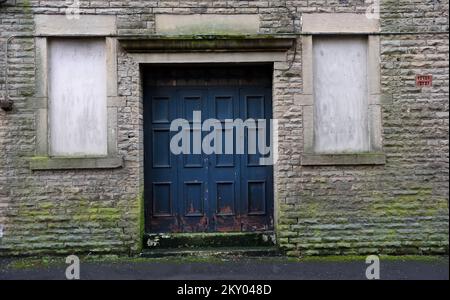 Blaue Tür alt und verwittert mit abblätternder Farbe in der Tür des Steinhauses mit verkleideten Fenstern und Moos bedeckt. Eintritt zum alten Tanz Stockfoto