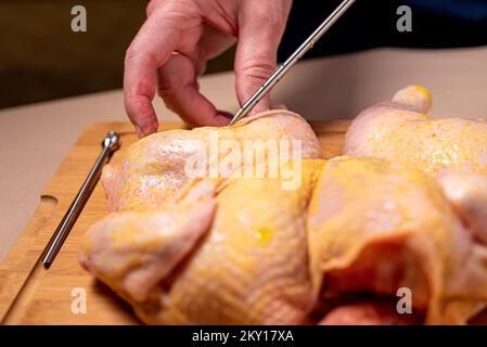 Der Küchenchef bereitet rohes Hähnchen in der Küche zu. Der Mensch bereitet rohes Hähnchen zum Grillen zu und injiziert dabei Cider in das Fleisch. Nahaufnahme. Stockfoto