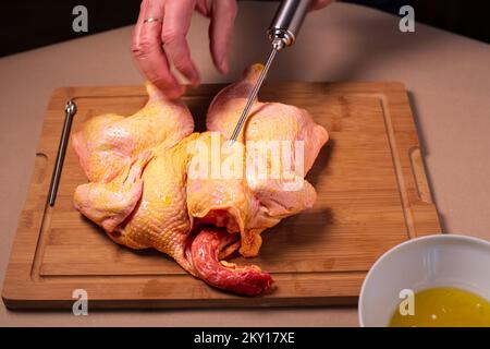 Der Küchenchef bereitet rohes Hähnchen in der Küche zu. Der Mensch bereitet rohes Hähnchen zum Grillen zu und injiziert dabei Cider in das Fleisch. Nahaufnahme. Stockfoto