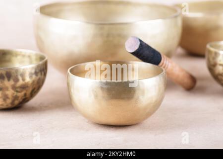 Tibetische Gesangsschüsseln mit Stöcken, die während Mantra-Meditationen auf beigefarbenem Steinhintergrund verwendet werden, Nahaufnahme. Schallheilende Musikinstrumente für die Meditation, Stockfoto