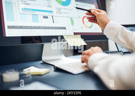 Unternehmerin, die mit Finanz- und Verkaufsdaten auf Diagrammen, Diagrammen und Diagrammen auf einem Computerbildschirm arbeitet. Frau sitzt am Schreibtisch im Büro Stockfoto