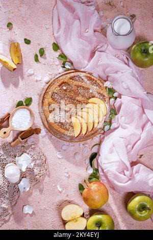 Köstlicher traditioneller Apfelkuchen mit geschnittenen Keilen und ganzen Apfelfrüchten auf Steinoberfläche, flach liegend. Draufsicht Stockfoto