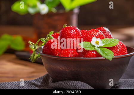 Erdbeeren in Tonschüssel auf einem Holztisch. Schüssel gefüllt mit saftig frischen reifen roten Erdbeeren. Selektiver Fokus Stockfoto