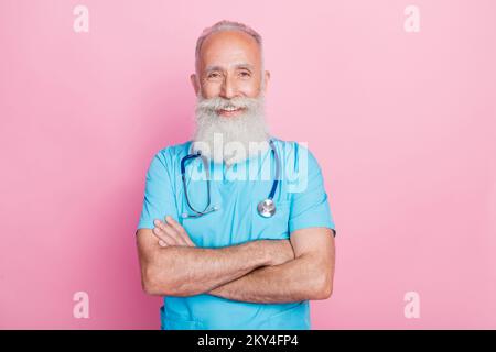 Foto eines professionellen Chirurgen, der die Arme kreuzte, um kranke Patienten auf pastellfarbenem Hintergrund zu untersuchen Stockfoto