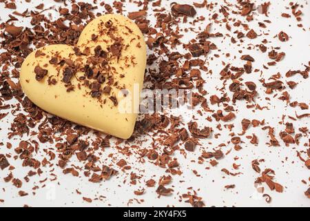 Blick auf ein weißes Schokoladenherz in Schokoladenchips auf weißem Hintergrund, Nahaufnahme. Valentinstagskonzept Stockfoto