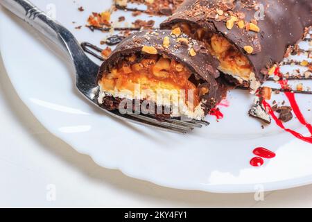 Dessertkuchen auf weißem Teller, Nahaufnahme, selektiver Fokus. Kuchen mit Schokolade und Nüssen bedeckt. Stillleben im Stil eines hohen Schlüssels Stockfoto