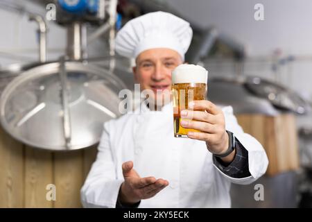 Der Braumeister hält ein Glas frisches, schaumiges, blasses Ale Stockfoto