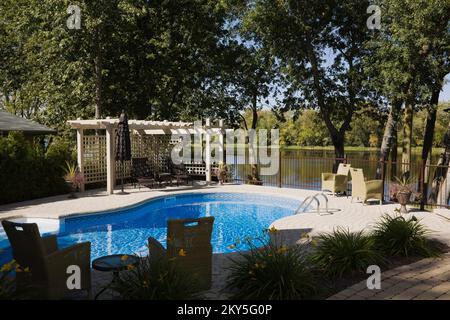 Im Sommer befindet sich ein Swimmingpool im Boden mit Gartenmöbeln im Garten. Stockfoto