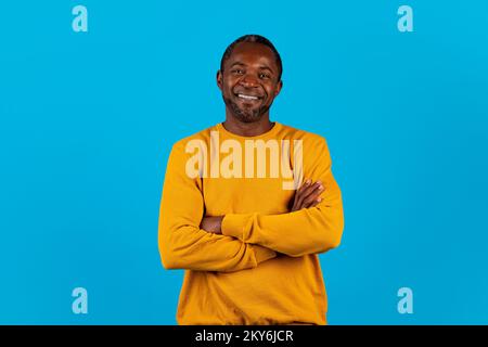 Selbstbewusster afroamerikanischer Mann, der über blauen Hintergrund lächelt Stockfoto