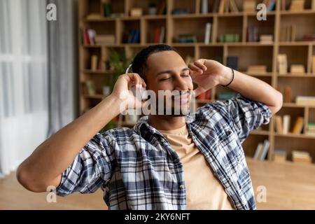 Freizeit zu Hause. Ruhiger araber, der mit geschlossenen Augen Musik über kabellose Kopfhörer hört und sich zu Hause entspannt Stockfoto