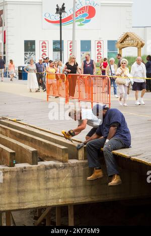 Atlantic City, N.J., 10. Juli, 2013 Monate, nachdem Hurrikan Sandy letzten Herbst auf Land ging, ersetzen zwei Arbeiter die von Sturm zerstoßenen Bretter von der Promenade von Atlantic City, Steel Pier. Hurrikan Sandy Aus New Jersey. Fotos zu Katastrophen- und Notfallmanagementprogrammen, Aktivitäten und Beamten Stockfoto
