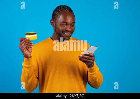 Ein lächelnder schwarzer Mann mit Smartphone und Kreditkarte Stockfoto