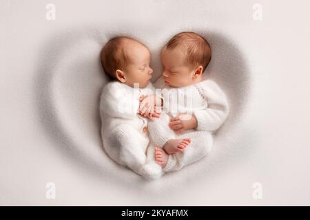 Winzige neugeborene Zwillingsjungen in weißen Bodys auf weißem Hintergrund. Stockfoto
