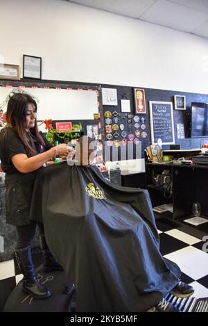 Frau Barbier und Friseurin schneiden einem kleinen schwarzen Jungen die Haare Stockfoto
