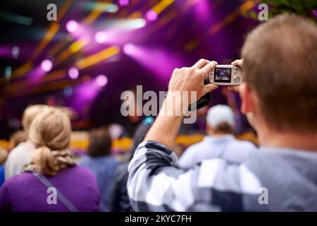 Leben mit Verschlusszeit. Rückansicht eines Mannes in der Menge, der eine Kamera hält, um ein Konzert zu fotografieren. Stockfoto