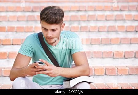 Wir treffen uns nach dem Unterricht. Ein junger Schüler, der auf der Treppe sitzt und SMS schreibt. Stockfoto