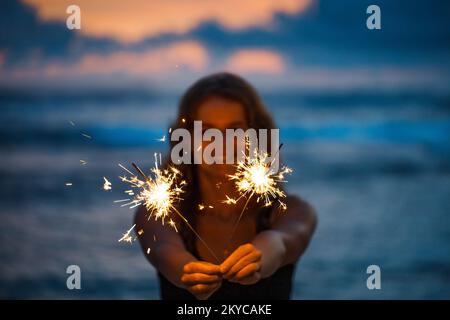 Eine junge Frau, die mit dem Sparkler Silvester am Strand feiert Stockfoto