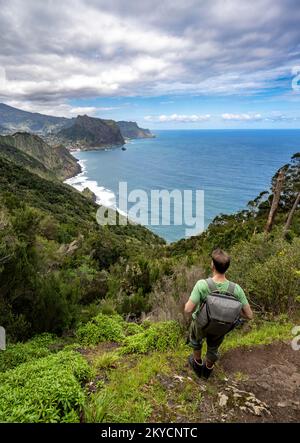 Wandern Sie in die Ferne, Blick auf die steile felsige Küste und das Meer, im Hintergrund Dorf Porto da Cruz und Adlerfelsen Penha de Aguia, Küste Stockfoto