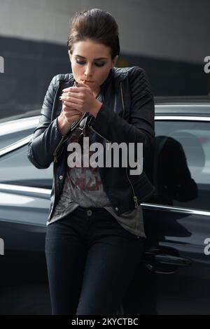 Eine rebellisch aussehende junge Frau, die in einer Garage eine Zigarette raucht. Stockfoto