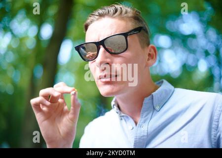 Mach einen Hit. Ein junger Mann, der einen Joint raucht, auf einem Fest im Freien. Stockfoto