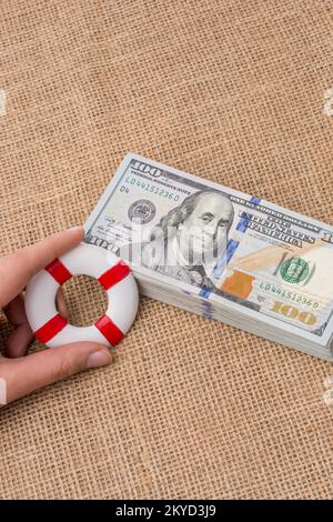 Rettungsring in der Hand über das Banknotenbündel aus US-Dollar Stockfoto