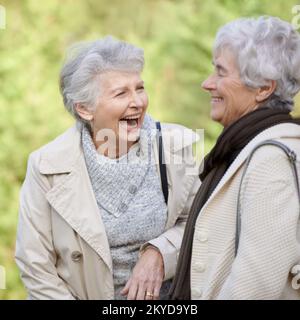 Sie sind immer noch beste Freunde. Kurzer Blick auf zwei alternde Seniorinnen, die im Freien lächeln und sich unterhalten. Stockfoto