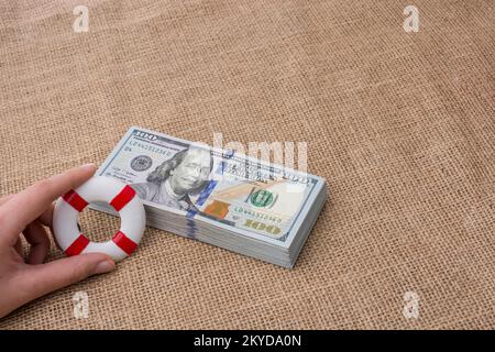 Rettungsring in der Hand über das Banknotenbündel aus US-Dollar Stockfoto