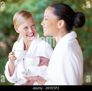 Schmeckt dieser Kräutertee gut oder was? Zwei junge Frauen trinken Kaffee im Bademäntel im Day Spa. Stockfoto