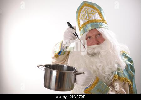 USA auf weißem Hintergrund. Holländischer Weihnachtsmann St. Nicholas weihnachten Neujahr St. Nicholas mit einem Topf in der Hand bereitet Silvester-Dinner Essen zu, das für Weihnachten wirbt Essen mit einer Schaufel essen Stockfoto