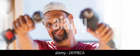 Ein männlicher Schmalzbauer bei der Arbeit. Nahaufnahme eines Arbeiters mit Bart und Mütze. Das Gesicht hat Werkzeuge, einen Schraubendreher und einen Bohrer. Hochwertiges Foto. Stockfoto