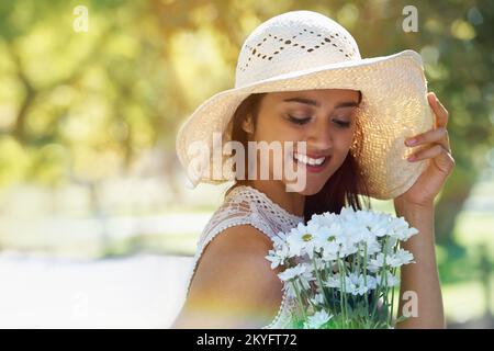 Der Frühling ist da. Eine junge Frau, die Blumen in der Hand hält und einen Sonnenhut trägt, während sie in einem Park steht. Stockfoto