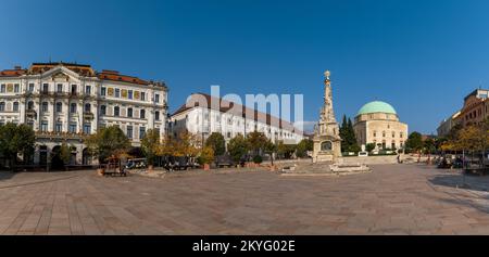 Pecs, Ungarn - 13. Oktober 2022: Blick auf den Szechenyi-Platz in der Innenstadt von Pécs mit der Statue der Heiligen Dreifaltigkeit und der Pascha-Qasim-Moschee Stockfoto