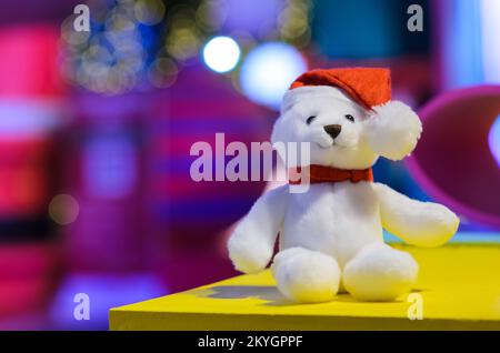 Selektiver Fokus auf den weihnachtsmann Teddybären, die einen Hut vor bunten, verschwommenen Hintergründen und Bokeh-Lichtern tragen. Stockfoto
