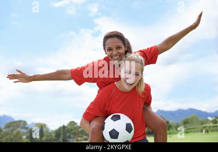 Wir feiern einen brillanten Streik. Eine Fußballspielerin, die ihre Teamkollegin bei der Feier auf dem Rücken trägt. Stockfoto