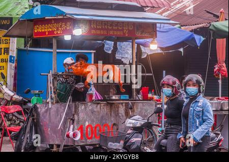 Zwei kambodschanische Frauen, die Gesichtsmasken tragen, warten auf ihr geröstetes Schweinefleisch während der COVID-19-Pandemie. Kandal Market, Phnom Penh, Kambodscha. © Kraig Stockfoto