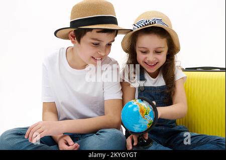 Glückliche Mädchen und Jungen zeigen mit der Erdkarte auf einen Ort auf der ganzen Welt und wählen ein neues Reiseziel für den Urlaub Stockfoto