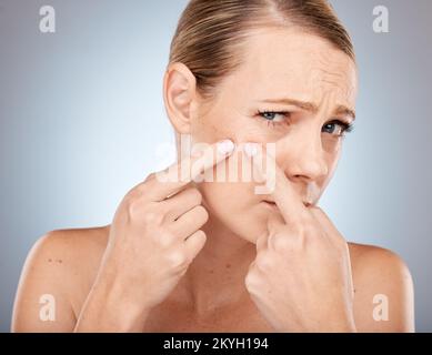 Gesicht, Hautpflege und Frauen drücken Akne, Pickel oder Schwarzkopf im Studio auf grauem Hintergrund. Wellness-, Dermatologie- und kosmetologische Porträts von SAD Stockfoto