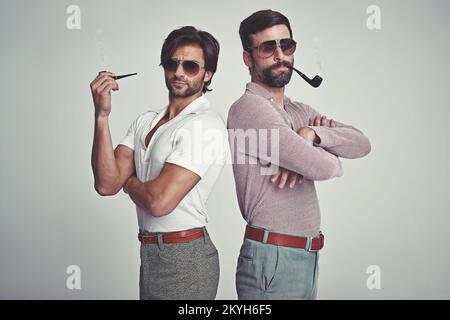 Sie haben sich weit aus Stil. Studioaufnahme von zwei Männern, die zusammen stehen, während sie Retro 70s tragen und Pfeifen rauchen. Stockfoto