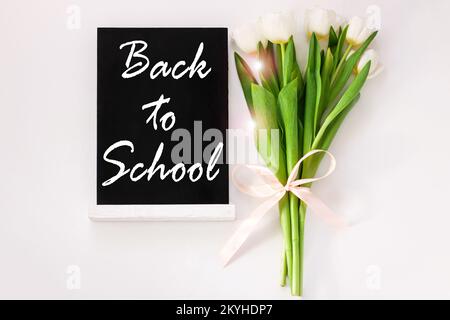 „Back to School“-Posterdesign mit Schild auf schwarzer Tafel und Tulpenblumen auf weißem Hintergrund. Nachricht auf der Tafel. Grußkarte i Stockfoto