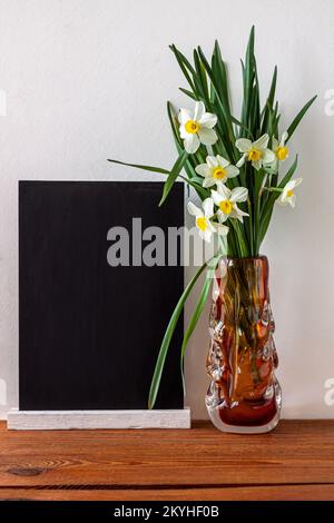 Schwarzes Kreidetafelmodell mit Narzissenblumen-Bouquet in einer Vase auf weißem Hintergrund. Menü an der Tafel mit Staffelei. Kopierbereich zum Hinzufügen von Text für den Verkauf Stockfoto