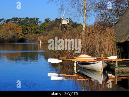 Blick auf den Fluss Ant an den Norfolk Broads im Herbst mit festgemachtem Ruderboot und Boardman's Mill in How Hill, Norfolk, England, Großbritannien. Stockfoto