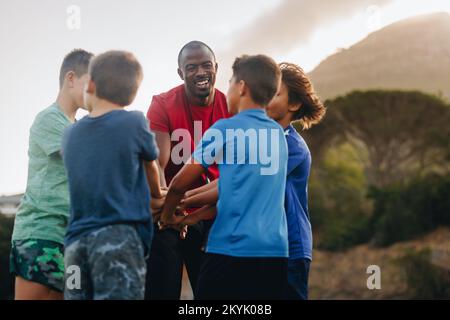 Rugby-Trainer und seine Schüler legen ihre Hände in einem Meeting zusammen. Sporttrainer, der seinem Team ein Motivationsgespräch auf einem Feld gibt. Mann als Mentor A Stockfoto