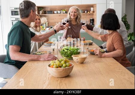 Group of diverse senior friends making a toast while having dinner at home Stockfoto