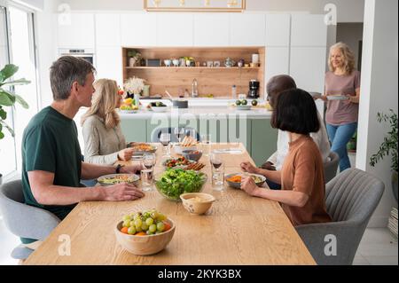 Group of diverse middle age friends gathered for dinner in kitchen Stockfoto