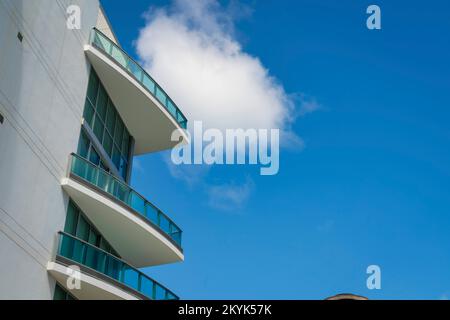 Blick auf dreieckige Balkone mit Glasgeländern von unten in Miami, Florida. Niedriger Blickwinkel auf ein Gebäude mit ausgekleideter Betonwand auf der linken Seite und b Stockfoto