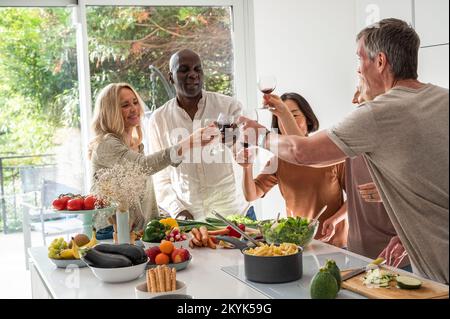 Diverse group of senior friends making a toast while gathered around kitchen island Stockfoto